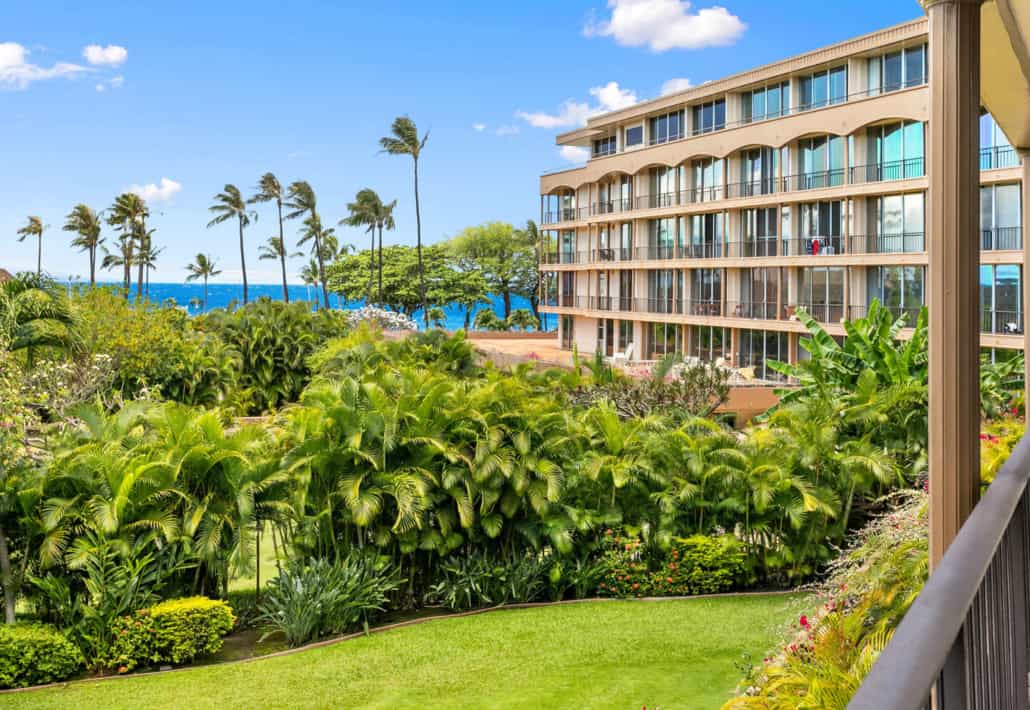 view of the property with lush tropical palm trees, green grass and views of the ocean
