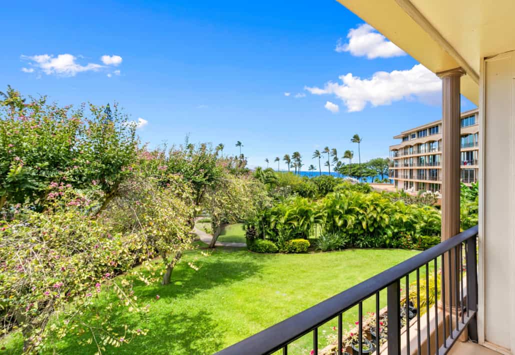 view of the property with lush tropical palm trees, green grass and views of the ocean