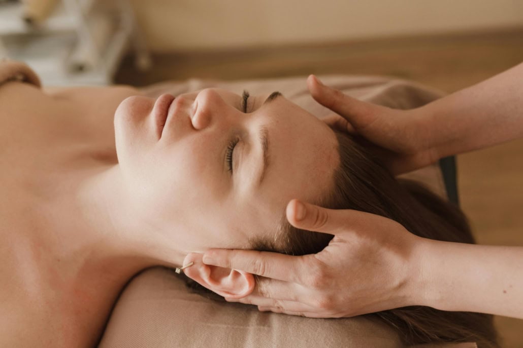 A woman with her eyes closed, facing up, while a masseuse massages her temples.