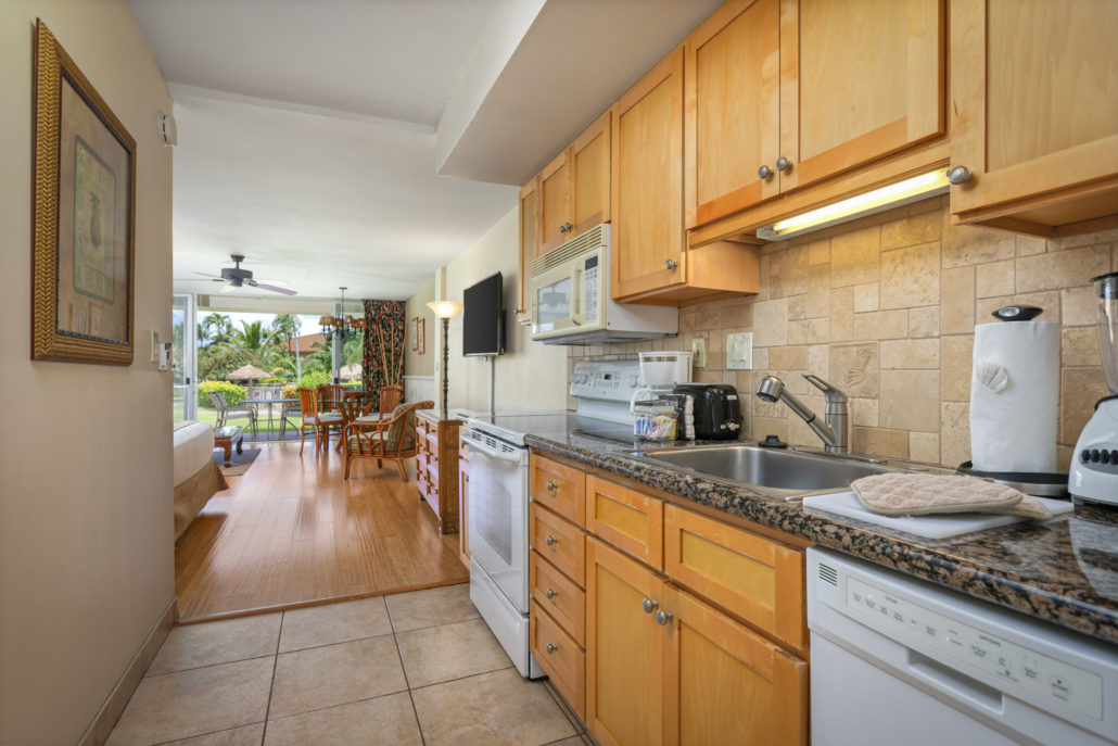 kitchen in a condo studio with full-stove, microwave, counter top appliances, telsision in the main room with a seprate dining area looking out to the covered lanai with seating