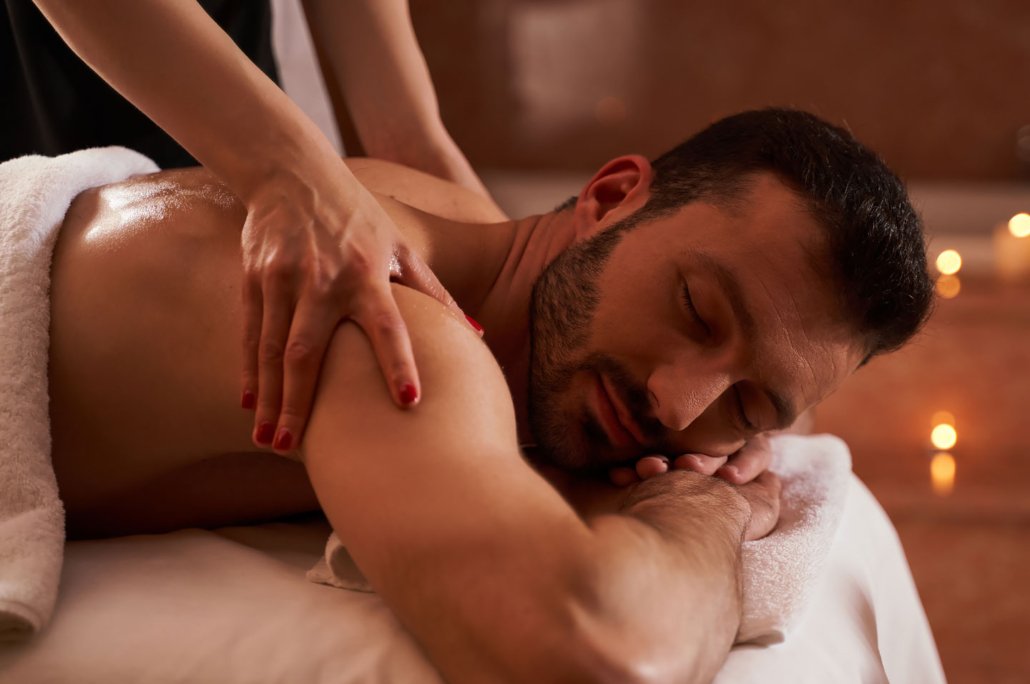 A man face down on a massage table with his hands under his face while a woman massages his shoulders.